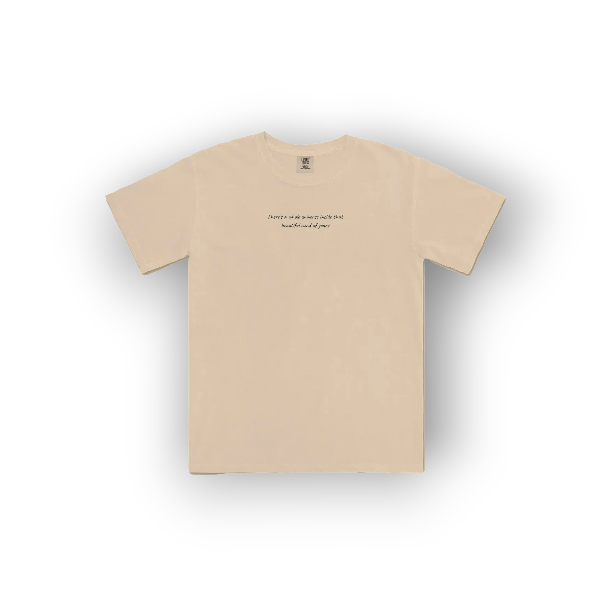 A beige crewneck t-shirt with a small black text graphic printed on the center chest, displayed flat against a white background with a soft drop shadow.