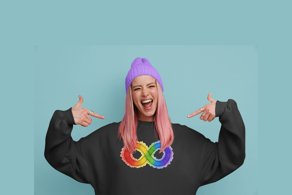 A person with pink hair and a purple beanie points inward with both hands while wearing a black sweatshirt with a rainbow infinity symbol on the chest, set against a solid light blue background.
