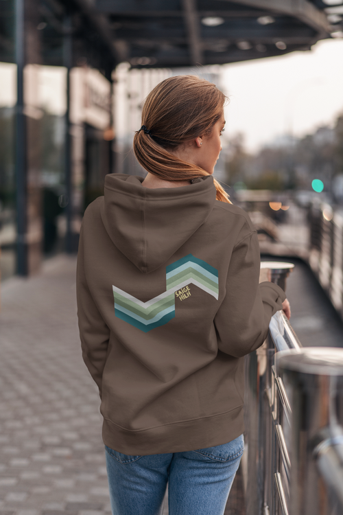 A woman viewed from behind wearing a brown hoodie with a large chevron graphic in shades of teal, green, and white on the back. The graphic features the text 'SAIGE HILH'.