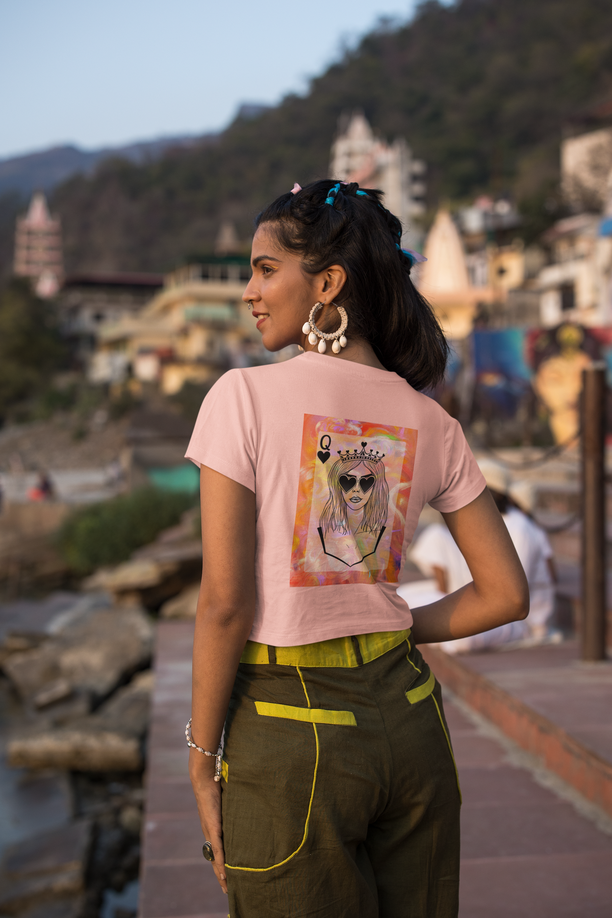 Woman standing infront of view with a large print on back of crop top t shirt. print is of a queen with a queen of hearts style Q in the top corner