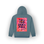 A slate blue hoodie shown from the back, featuring a large square graphic print with a pink and orange floral background and the text 'THIS TOO SHALL PASS' in dark blue lettering.