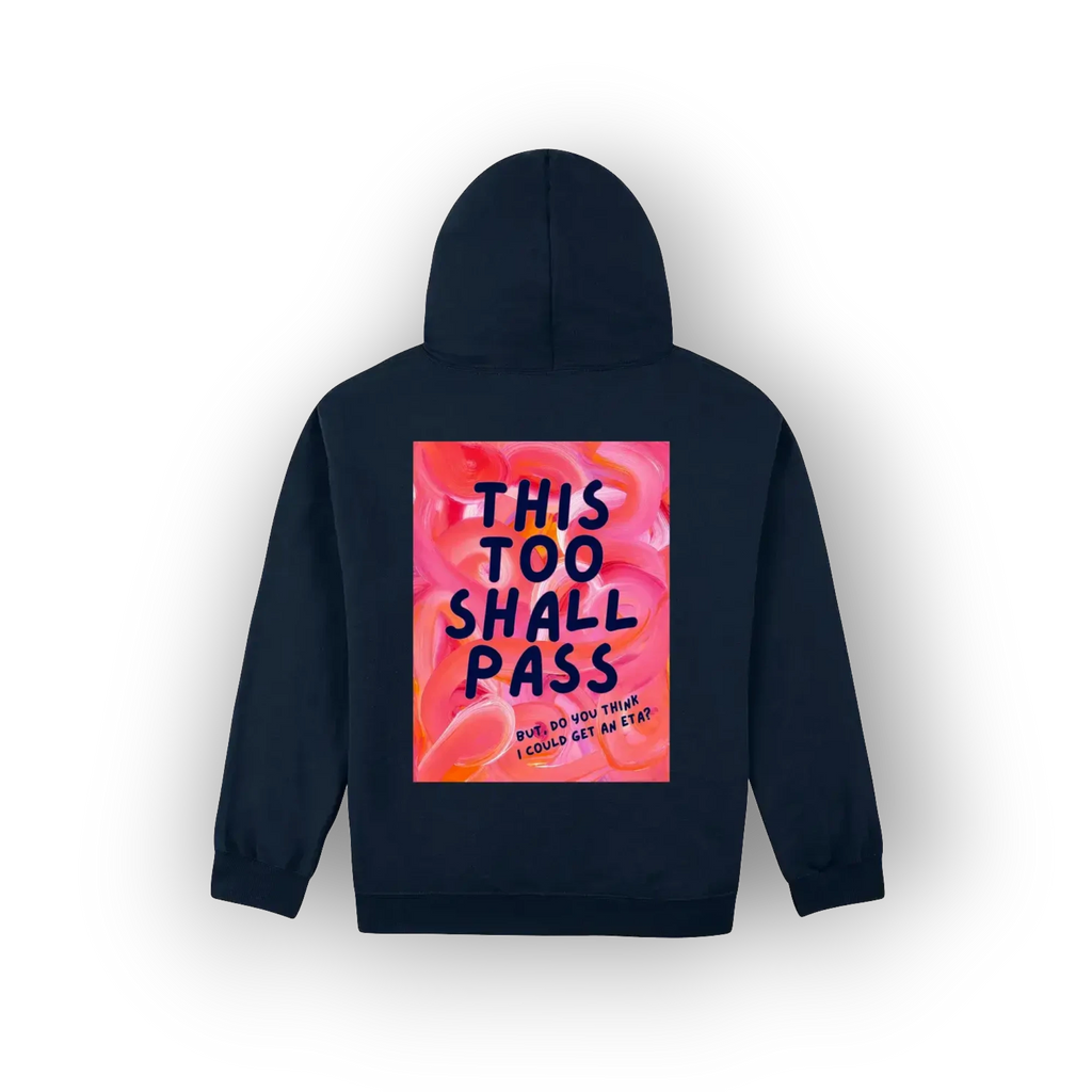 A navy blue hoodie shown from the back, featuring a large square graphic print with a pink and orange floral background and the text 'THIS TOO SHALL PASS' in dark blue lettering.