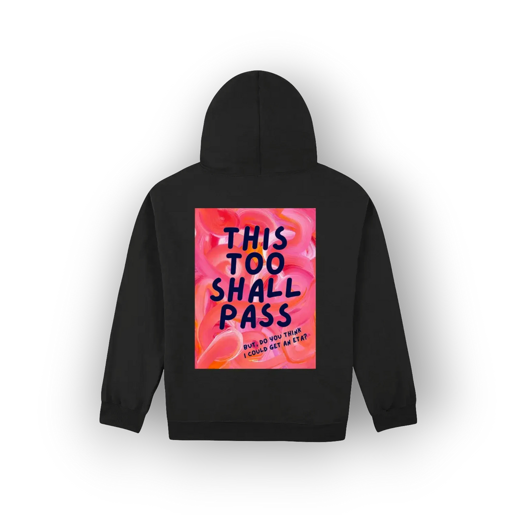 A black pullover hoodie shown from the back, featuring a large square graphic print with the text 'THIS TOO SHALL PASS' in dark blue lettering over a pink and orange floral background.