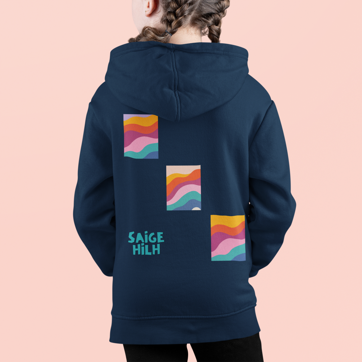 A child shown from the back wearing a navy hoodie with three colorful abstract wave graphics and the text 'SAIGE HILH' printed on the back, against a solid pale pink background.