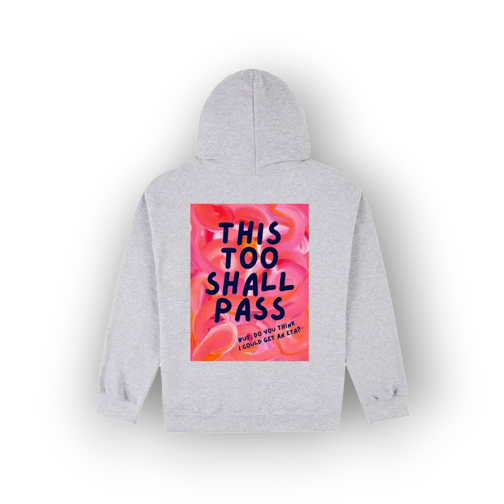 A light gray pullover hoodie shown from the back, featuring a large rectangular graphic print on the back. The graphic has a pink and orange floral background with the text 'THIS TOO SHALL PASS' in dark blue lettering.