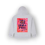 A light gray pullover hoodie shown from the back, featuring a large rectangular graphic print on the back. The graphic has a pink and orange floral background with the text 'THIS TOO SHALL PASS' in dark blue lettering.